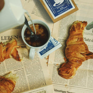 Löslicher Kaffee in Tasse mit Croissant und Zeitung