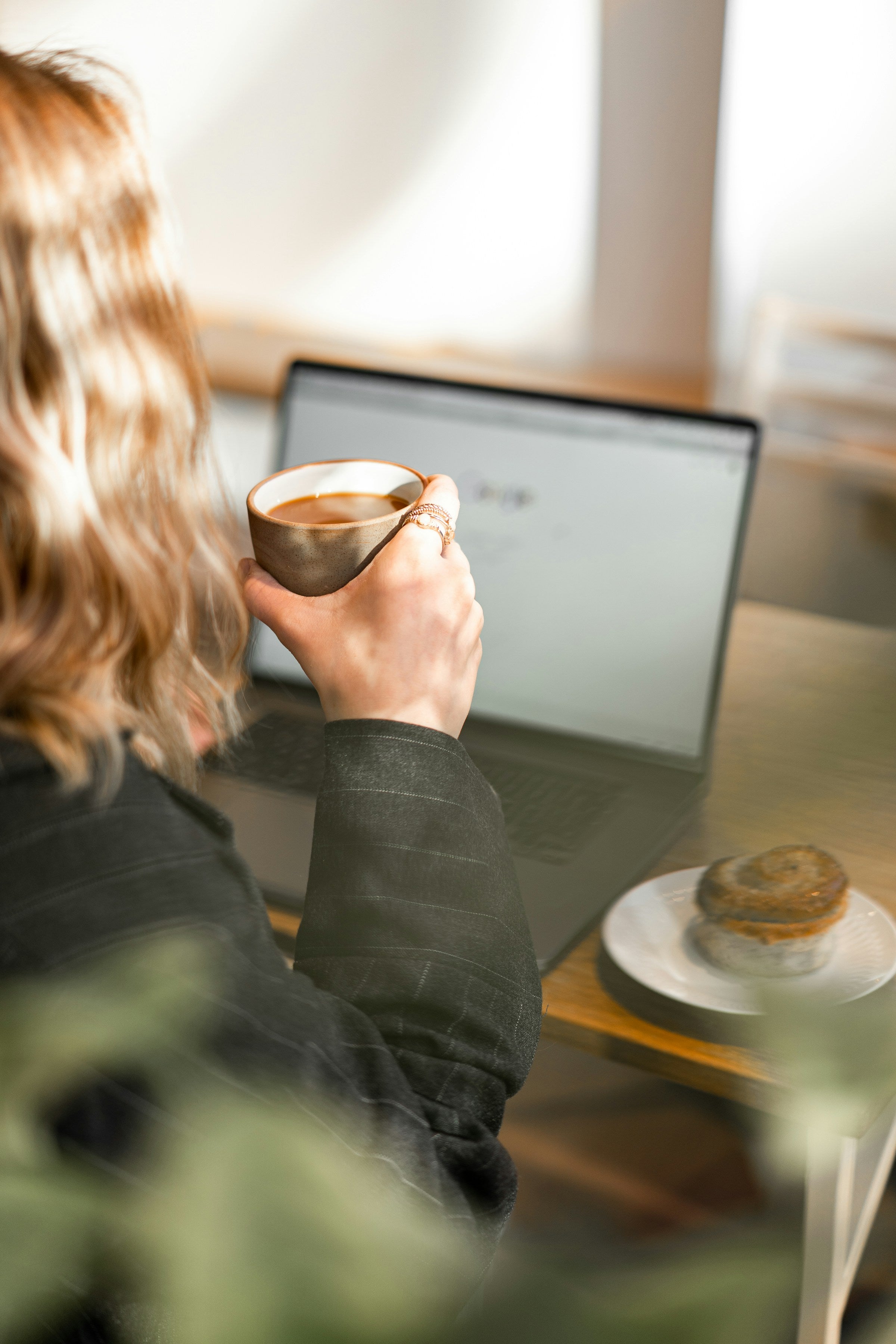 Frau hält Kaffeetasse in der Hand, vor dem Laptop sitzend