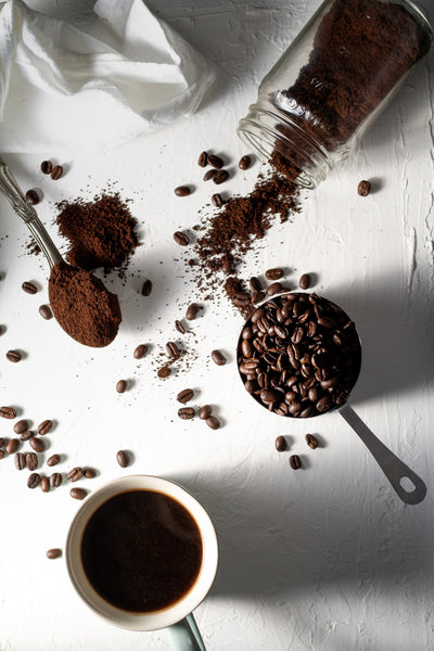 Löffel mit Kaffeebohnen und kleiner Löffel mit gemahlenem Kaffee neben Kaffeetasse mit Filterkaffee