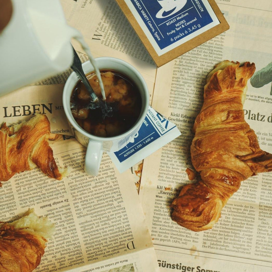 Löslicher Kaffee in Tasse mit Croissant und Zeitung