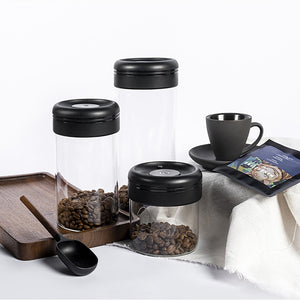 Timemore Glass Canister mit Kaffeebohnen, Kaffeetasse und -löffel im Hintergrund